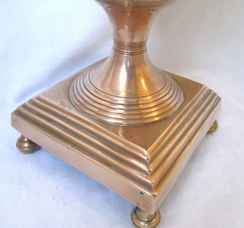 An early nineteenth-century copper tea urn featuring loop handles, a brass spigot, a decorative finial, and a square stepped pedestal base. View VII