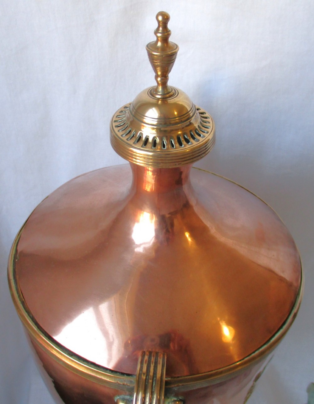An early nineteenth-century copper tea urn featuring loop handles, a brass spigot, a decorative finial, and a square stepped pedestal base. View X