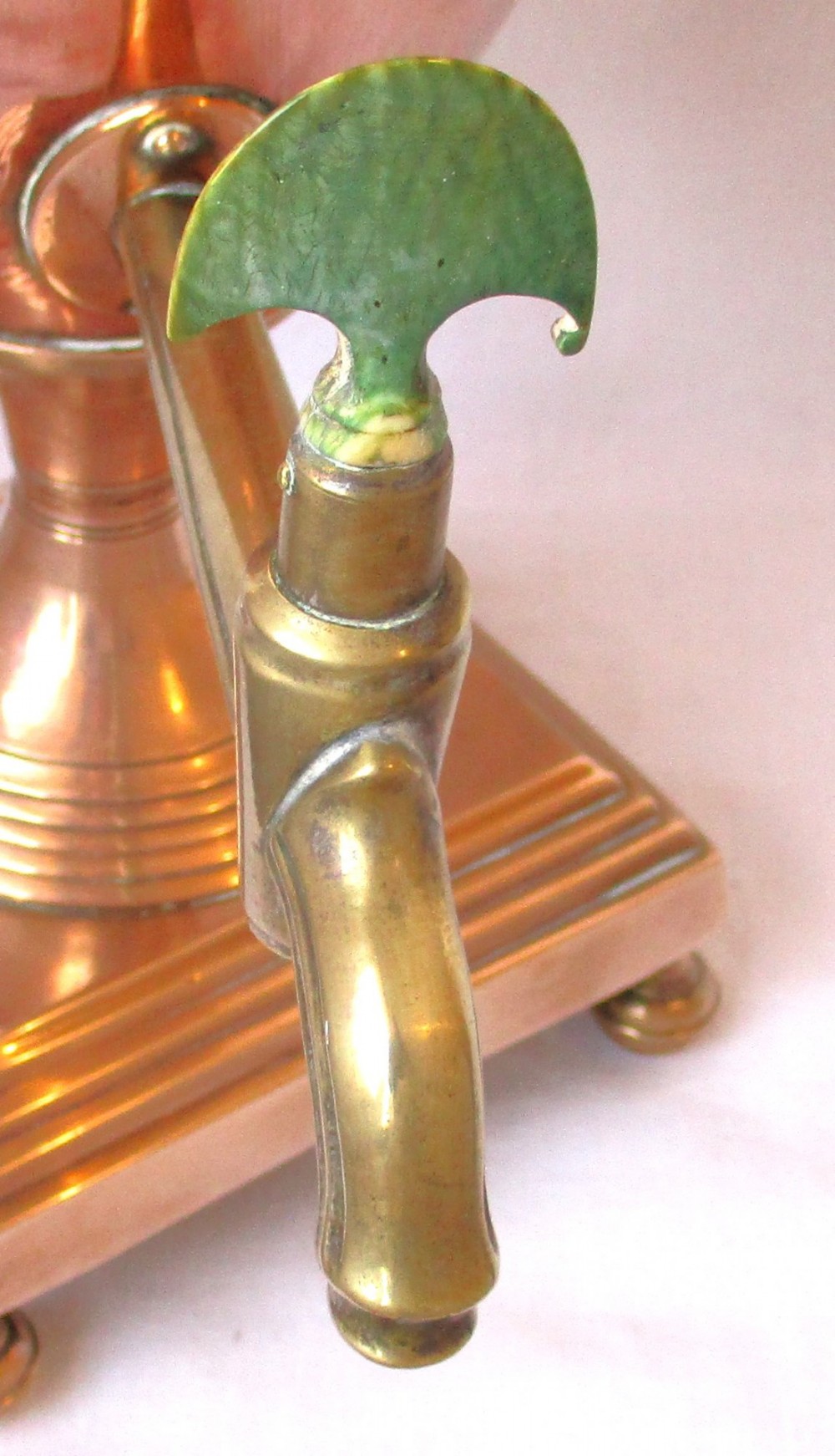 An early nineteenth-century copper tea urn featuring loop handles, a brass spigot, a decorative finial, and a square stepped pedestal base. View XI