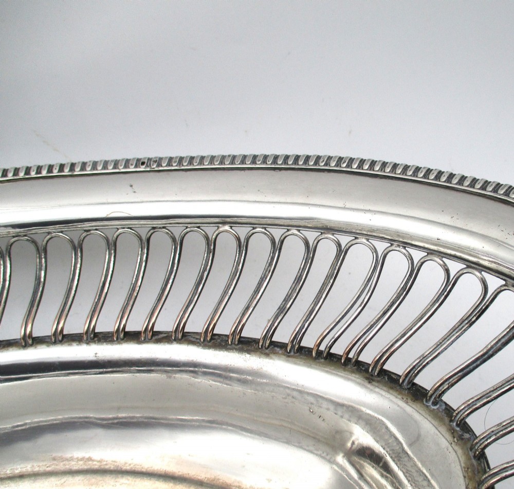 An oval Old Sheffield plate silver basket featuring an openwork wirework gallery, a beaded rim, and an overhead swing handle. View V