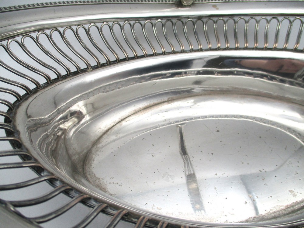 An oval Old Sheffield plate silver basket featuring an openwork wirework gallery, a beaded rim, and an overhead swing handle. View VI