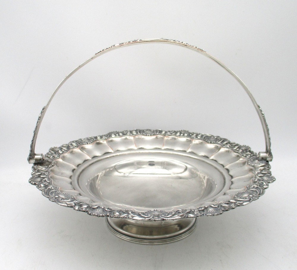 A round Old Sheffield Plate silver basket with a fluted rim, shell border motifs, an engraved crest, and a overhead swing handle. View II