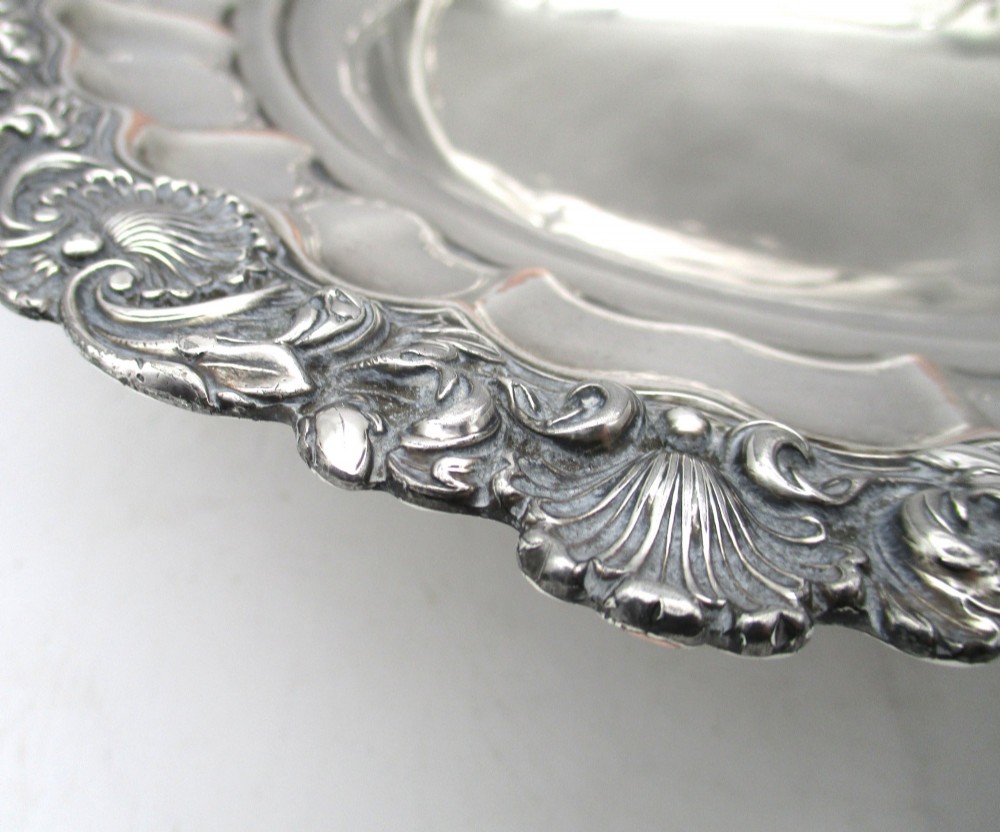 A round Old Sheffield Plate silver basket with a fluted rim, shell border motifs, an engraved crest, and a overhead swing handle. View V