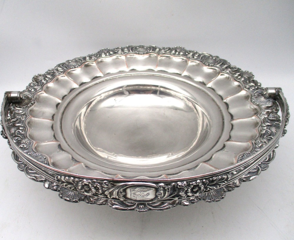 A round Old Sheffield Plate silver basket with a fluted rim, shell border motifs, an engraved crest, and a overhead swing handle. View VI