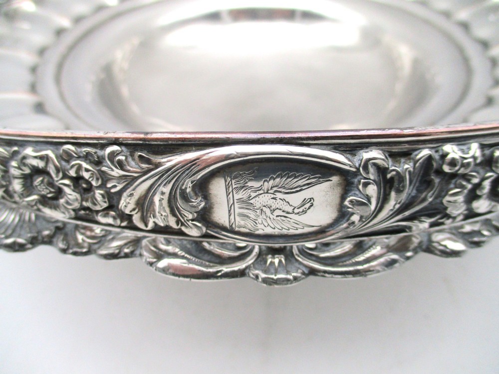 A round Old Sheffield Plate silver basket with a fluted rim, shell border motifs, an engraved crest, and a overhead swing handle. View VII