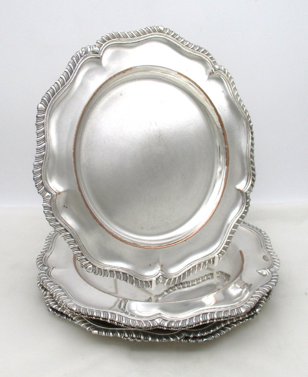 A stack of silver-plated dinner plates displaying scalloped, gadrooned borders with subtle copper show-through along the inner rims. View II