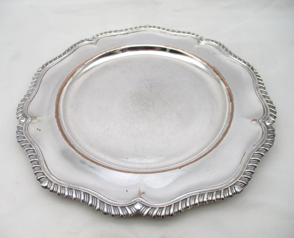 A stack of silver-plated dinner plates displaying scalloped, gadrooned borders with subtle copper show-through along the inner rims. View III