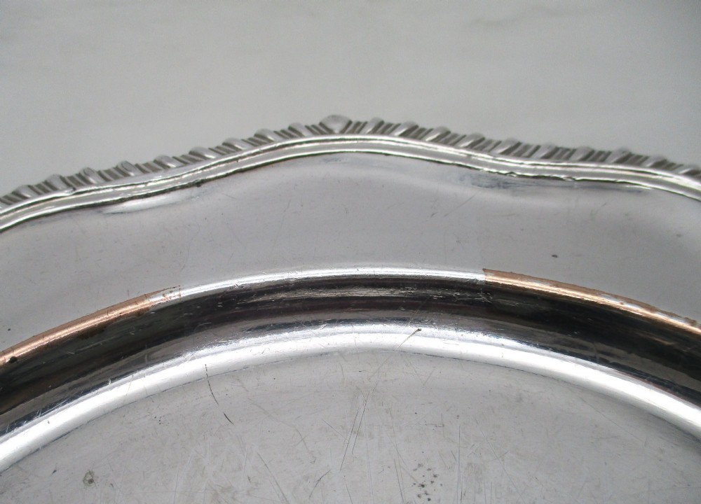 A stack of silver-plated dinner plates displaying scalloped, gadrooned borders with subtle copper show-through along the inner rims. View IV