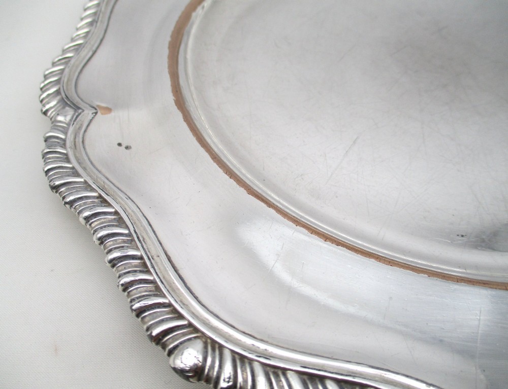A stack of silver-plated dinner plates displaying scalloped, gadrooned borders with subtle copper show-through along the inner rims. View V