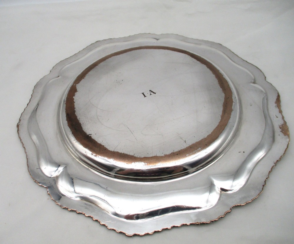 A stack of silver-plated dinner plates displaying scalloped, gadrooned borders with subtle copper show-through along the inner rims. View VI