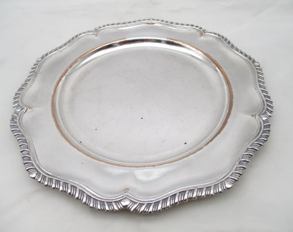 A stack of silver-plated dinner plates displaying scalloped, gadrooned borders with subtle copper show-through along the inner rims. View IX