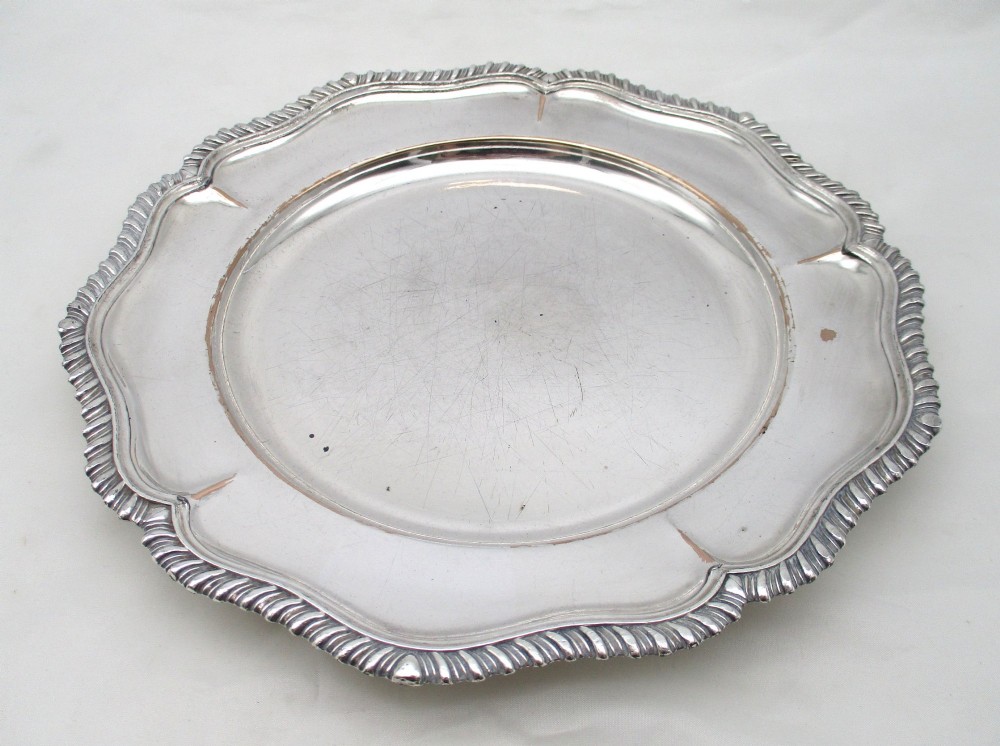 A stack of silver-plated dinner plates displaying scalloped, gadrooned borders with subtle copper show-through along the inner rims. View X