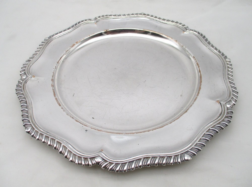 A stack of silver-plated dinner plates displaying scalloped, gadrooned borders with subtle copper show-through along the inner rims. View XII