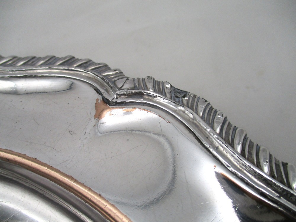 A stack of silver-plated dinner plates displaying scalloped, gadrooned borders with subtle copper show-through along the inner rims. View XIV