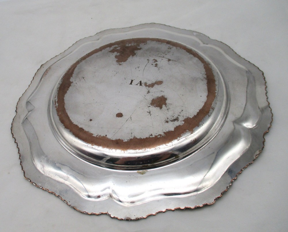 A stack of silver-plated dinner plates displaying scalloped, gadrooned borders with subtle copper show-through along the inner rims. View XV