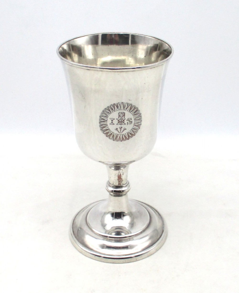 A 19th-century silver-plated church chalice featuring a flared cup with an engraved IHS Christogram medallion, a knopped stem, and a stepped circular base.