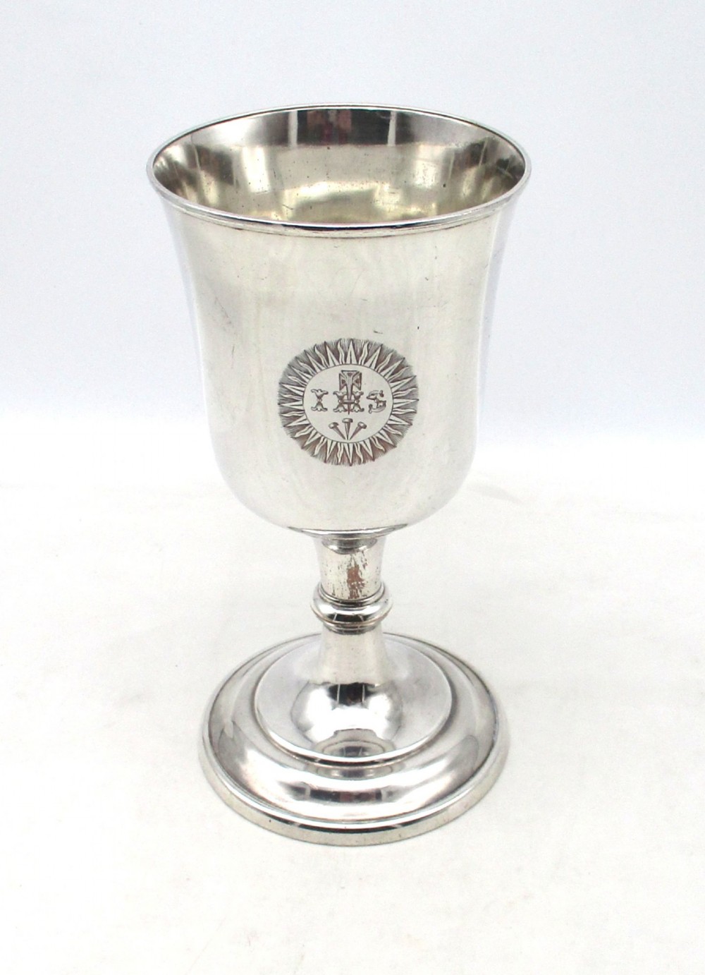 A 19th-century silver-plated church chalice featuring a flared cup with an engraved IHS Christogram medallion, a knopped stem, and a stepped circular base. View II