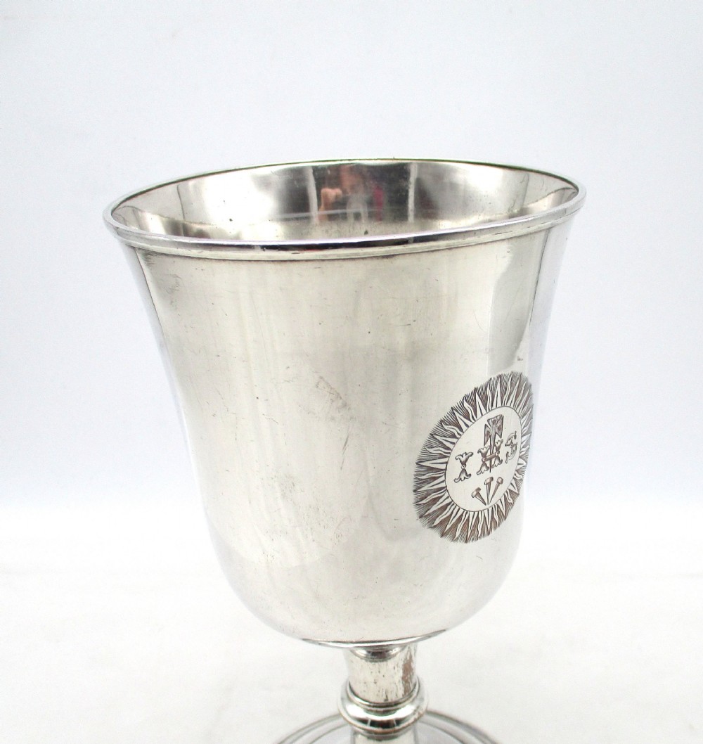 A 19th-century silver-plated church chalice featuring a flared cup with an engraved IHS Christogram medallion, a knopped stem, and a stepped circular base. View V