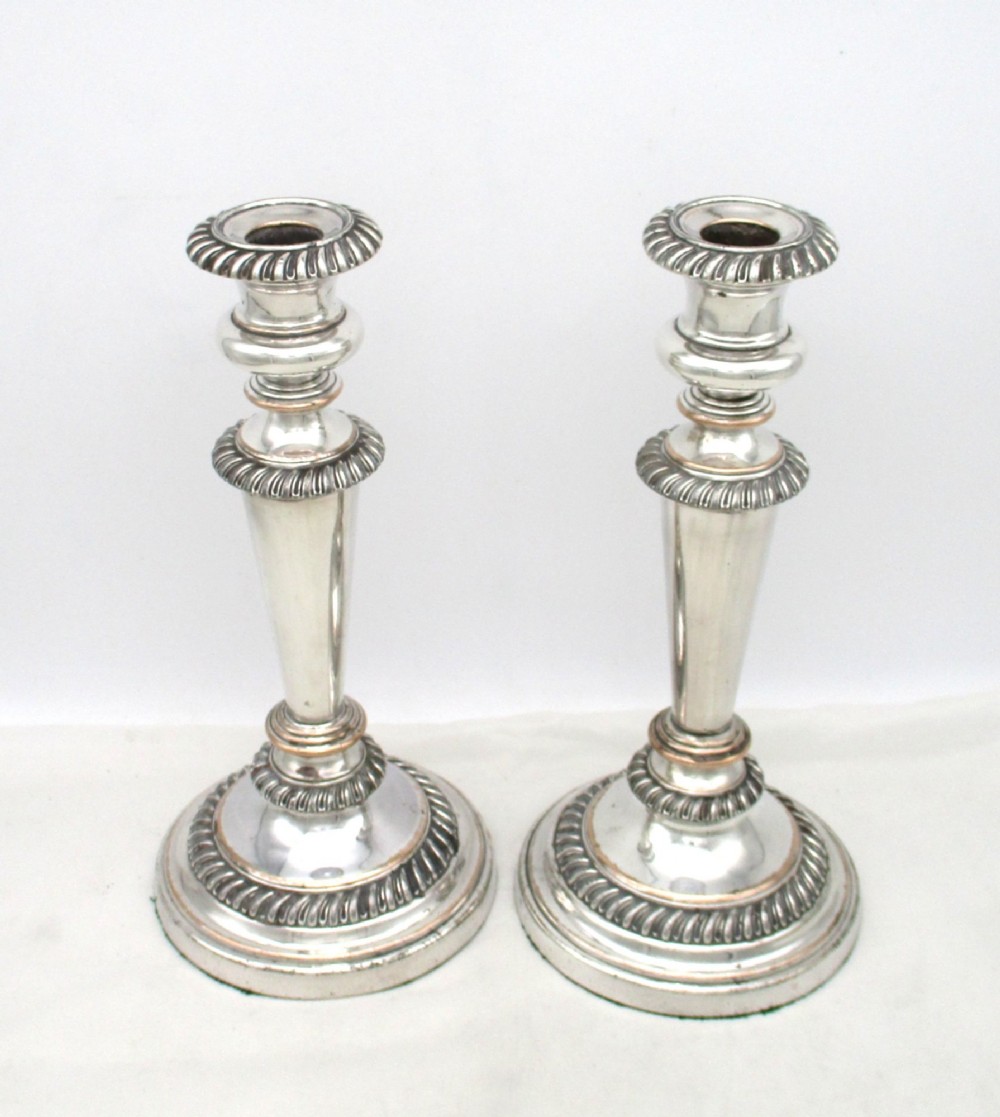 A pair of antique silver-plated candlesticks featuring gadrooned borders, tapered central stems, and circular bases.