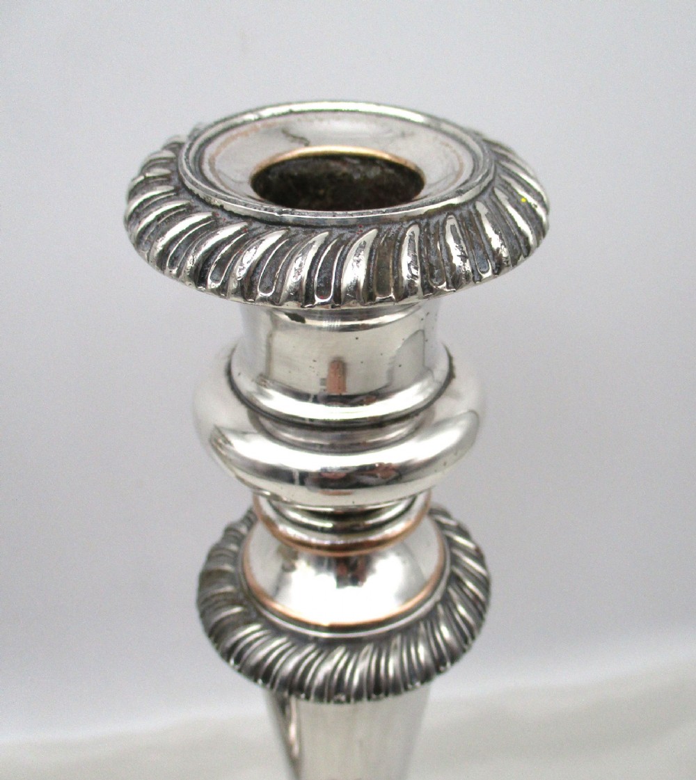 A pair of antique silver-plated candlesticks featuring gadrooned borders, tapered central stems, and circular bases. View IV