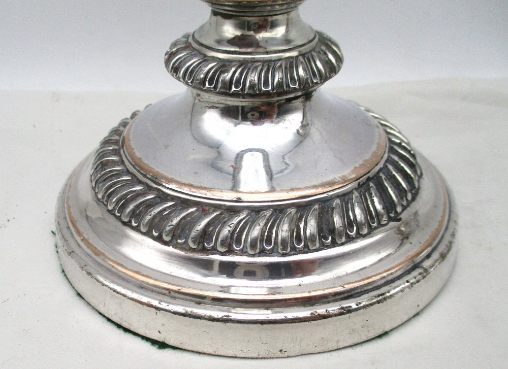 A pair of antique silver-plated candlesticks featuring gadrooned borders, tapered central stems, and circular bases. View V