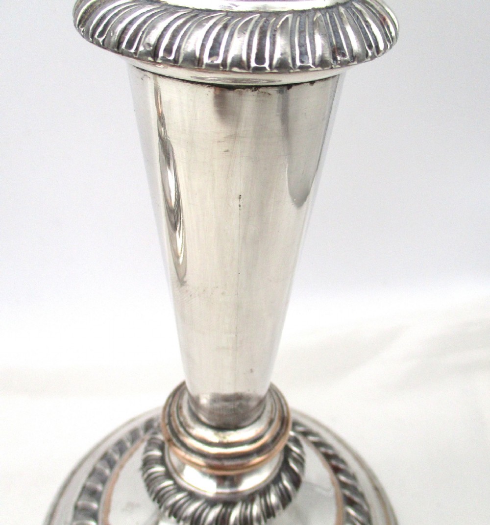 A pair of antique silver-plated candlesticks featuring gadrooned borders, tapered central stems, and circular bases. View VI