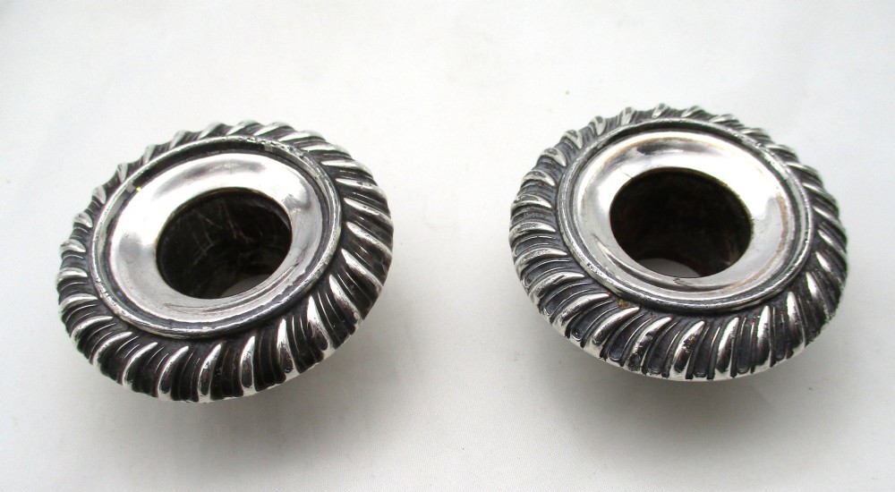 A pair of antique silver-plated candlesticks featuring gadrooned borders, tapered central stems, and circular bases. View IX