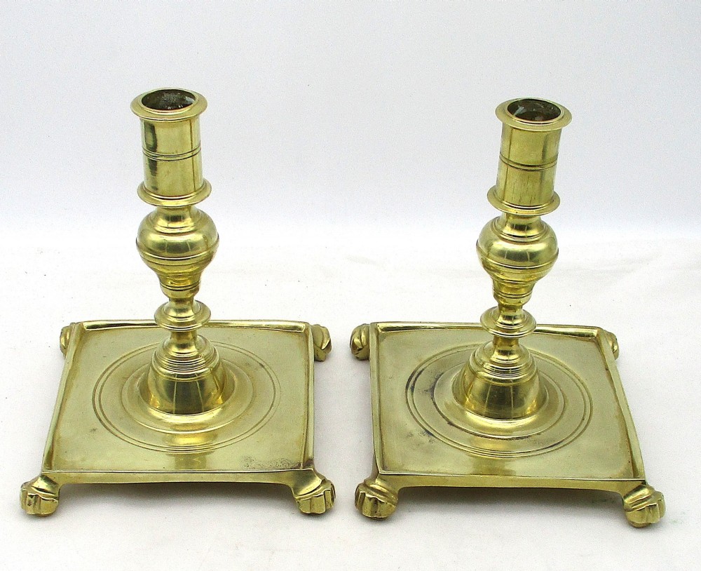 A pair of polished brass candlesticks with turned baluster stems and square bases featuring corner feet. View II
