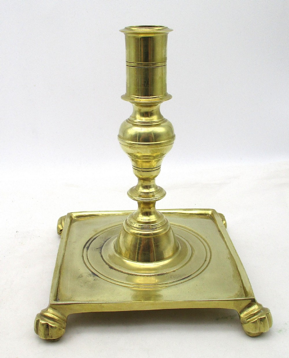 A pair of polished brass candlesticks with turned baluster stems and square bases featuring corner feet. View III