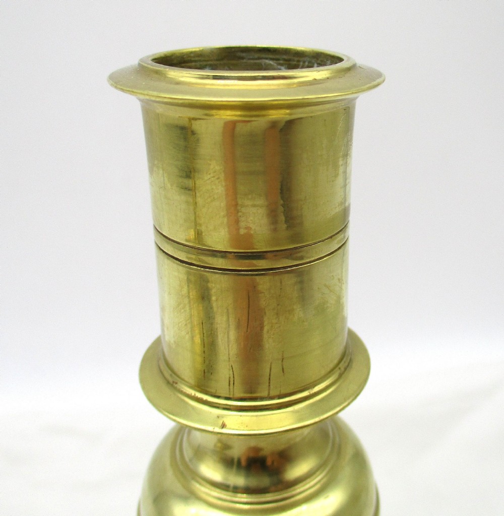 A pair of polished brass candlesticks with turned baluster stems and square bases featuring corner feet. View V