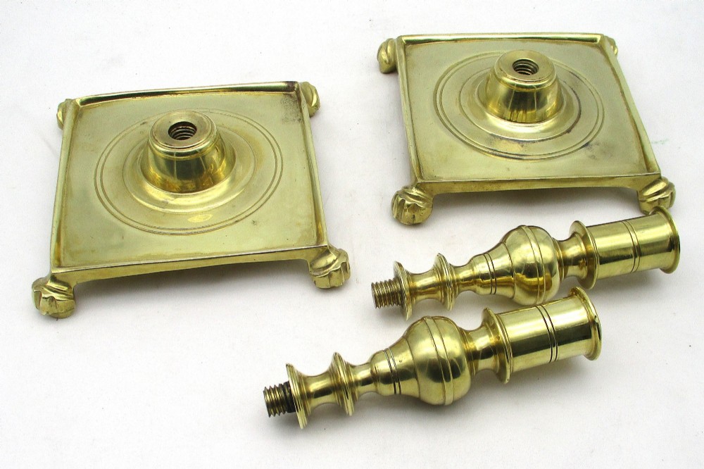 A pair of polished brass candlesticks with turned baluster stems and square bases featuring corner feet. View IX