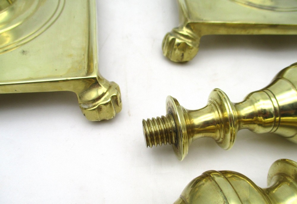A pair of polished brass candlesticks with turned baluster stems and square bases featuring corner feet. View X