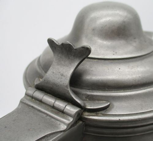A pair of matching 19th-century pewter communion flagons featuring domed hinged lids, thumbpiece levers, scroll handles, and engraved inscriptions on the cylindrical bodies. View V