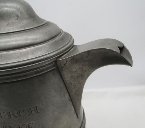 A pair of matching 19th-century pewter communion flagons featuring domed hinged lids, thumbpiece levers, scroll handles, and engraved inscriptions on the cylindrical bodies. View VII