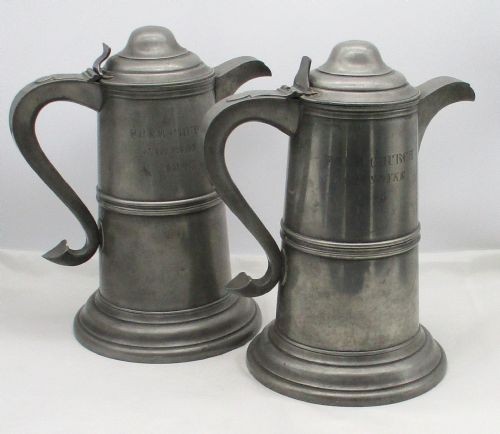 A pair of matching 19th-century pewter communion flagons featuring domed hinged lids, thumbpiece levers, scroll handles, and engraved inscriptions on the cylindrical bodies. View XIII