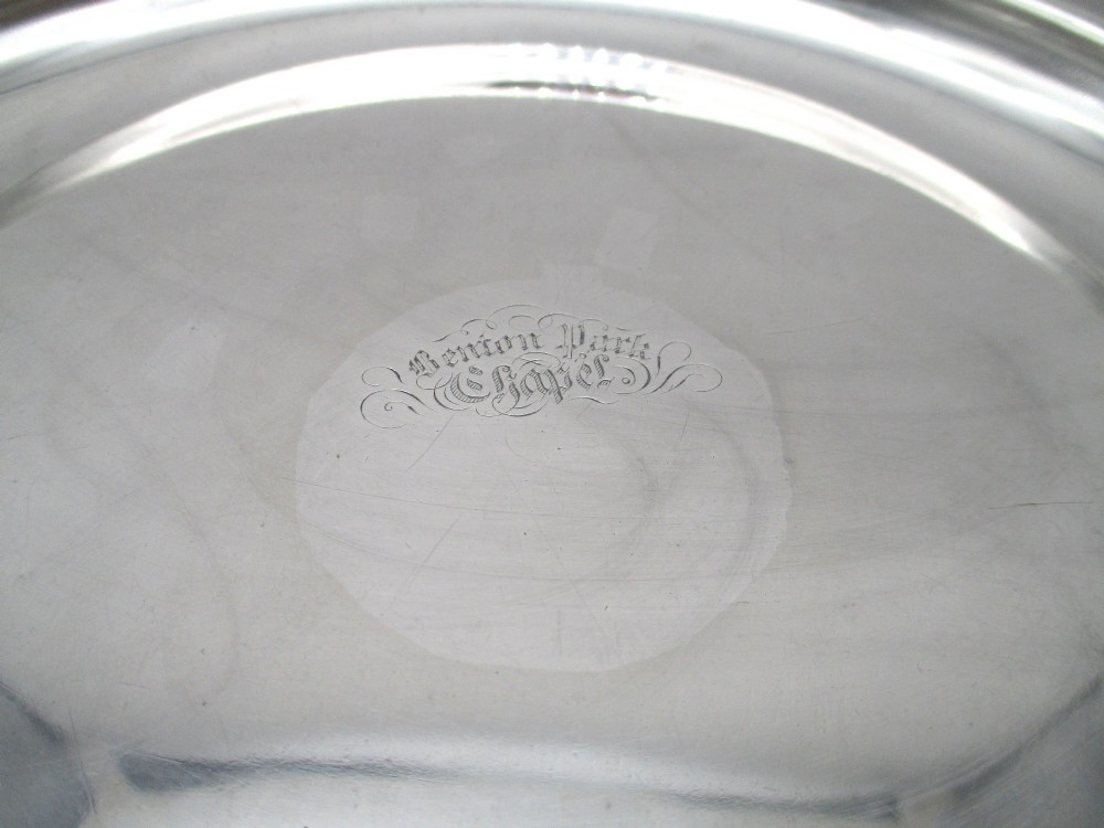 A pair of silver-plated communion plates featuring shaped scalloped rims with decorative relief detailing and engraved central crests. View III