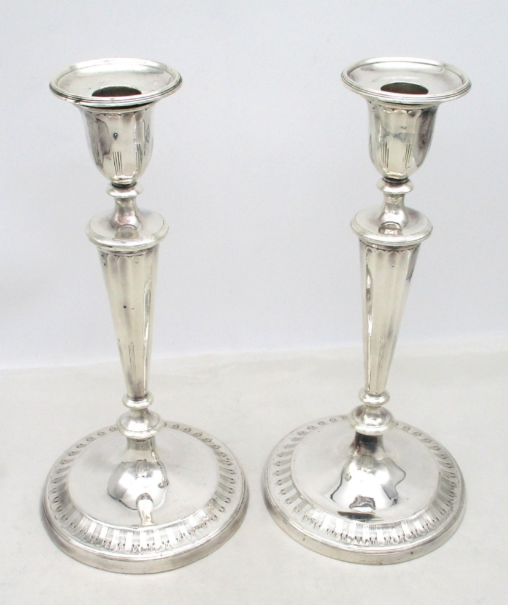 A pair of 19th-century silver-plated candlesticks featuring fluted tapered stems, urn-form sconces, and circular stepped bases.