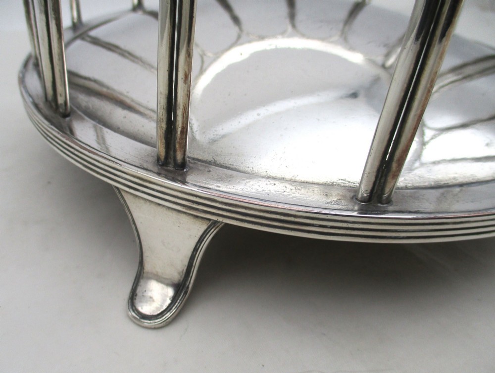 A silver-plated cylindrical bottle coaster featuring arched wirework sides, twin looped handles, a reeded rim, and small curved feet. View III