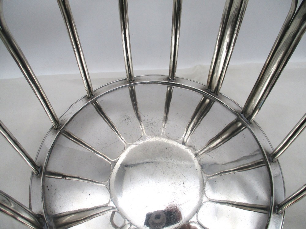 A silver-plated cylindrical bottle coaster featuring arched wirework sides, twin looped handles, a reeded rim, and small curved feet. View VIII