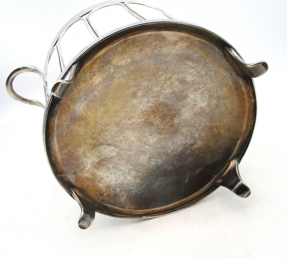 A silver-plated cylindrical bottle coaster featuring arched wirework sides, twin looped handles, a reeded rim, and small curved feet. View IX