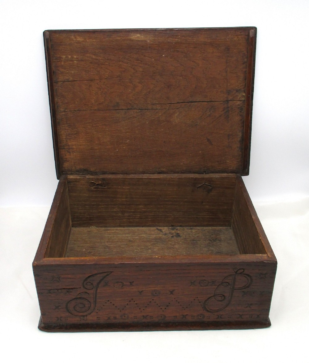 A rectangular dark oak document box featuring carved initials and geometric chip-carved detailing across the front panel. View V