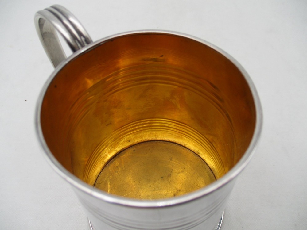 A Regency period Old Sheffield Plate childs tankard featuring horizontal reeded banding, a curved handle, and a gilt-lined interior. View V