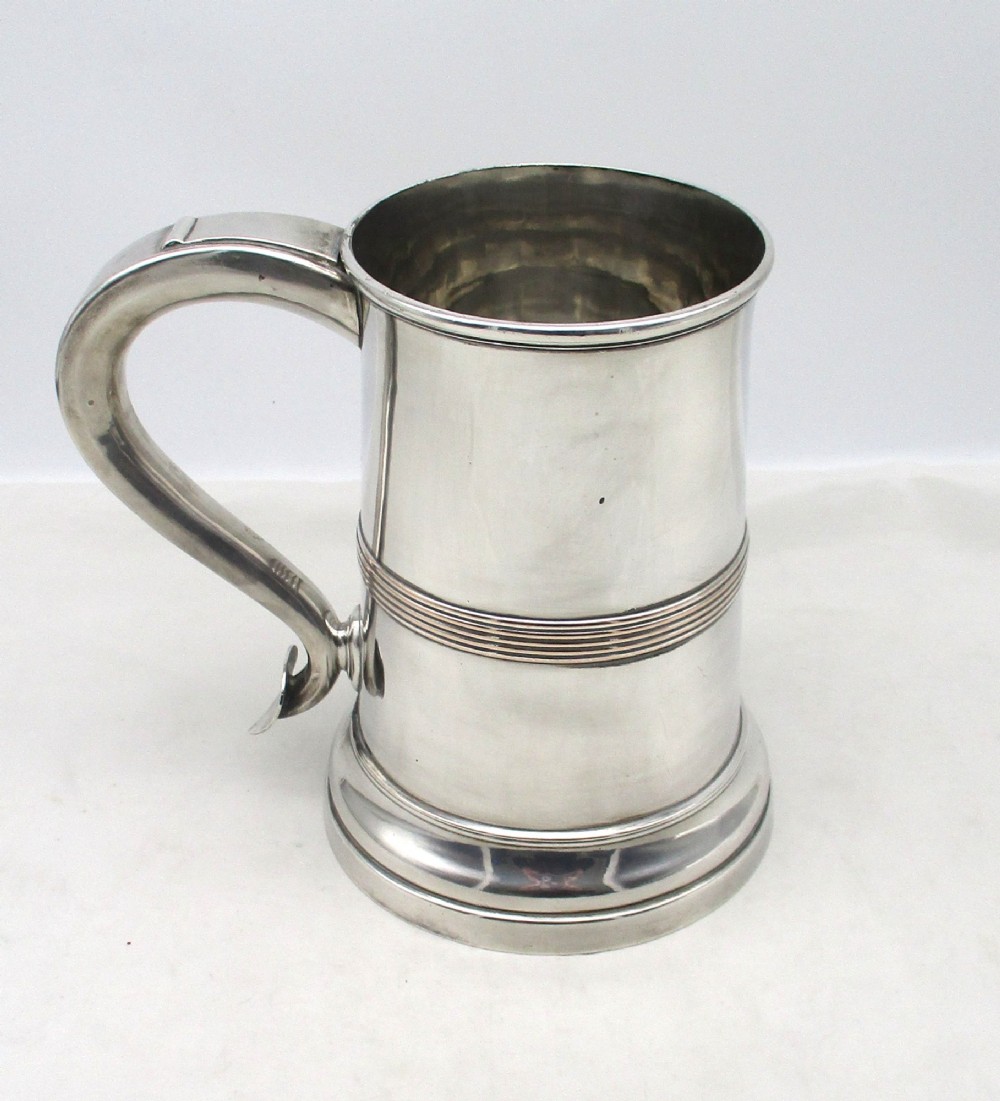 A Georgian Old Sheffield plated silver tankard featuring a reeded central band, a curved handle, and a stepped circular base.