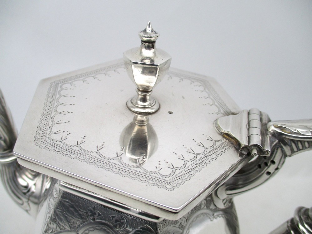 An octagonal silver plated teapot featuring floral engravings, a stylised handle with insulators, a shaped spout, and a finial lid. View IV