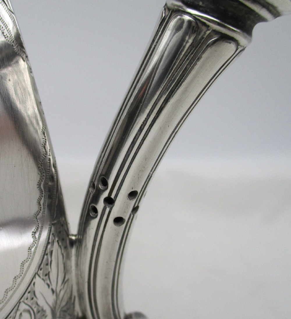 An octagonal silver plated teapot featuring floral engravings, a stylised handle with insulators, a shaped spout, and a finial lid. View VI