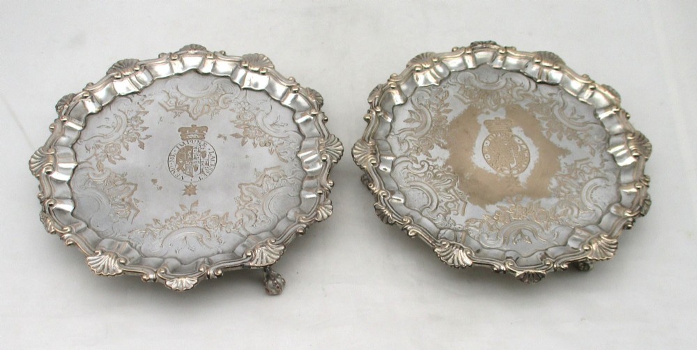 A pair of circular 18th-century Old Sheffield plated card trays with shell borders, heraldic crest engravings, and small scroll feet.