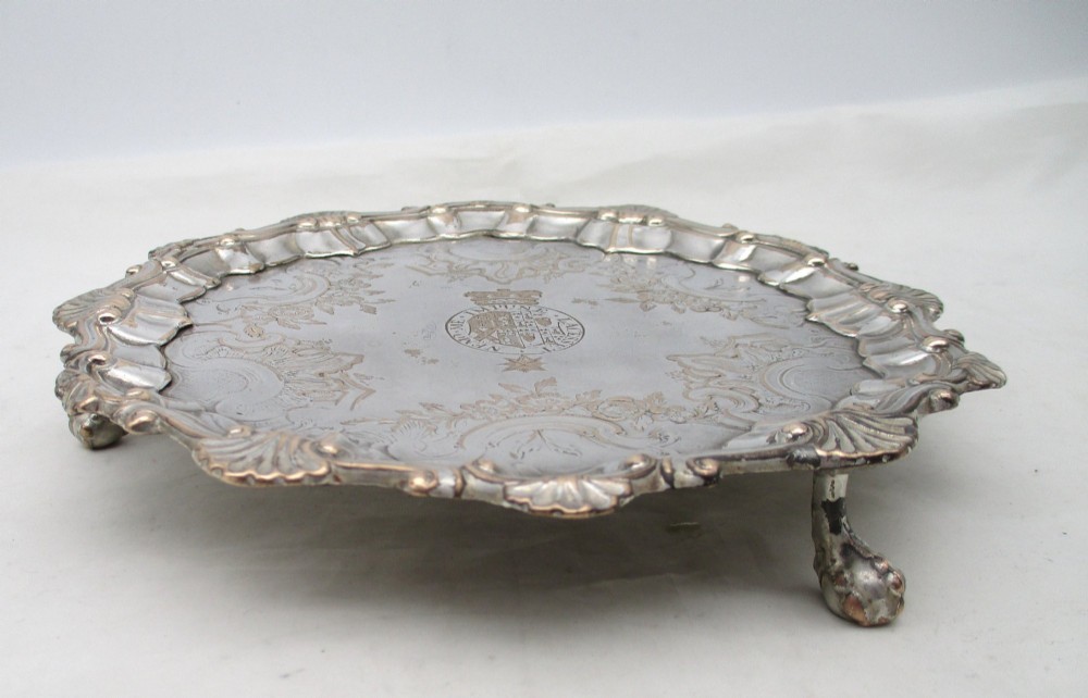 A pair of circular 18th-century Old Sheffield plated card trays with shell borders, heraldic crest engravings, and small scroll feet. View V