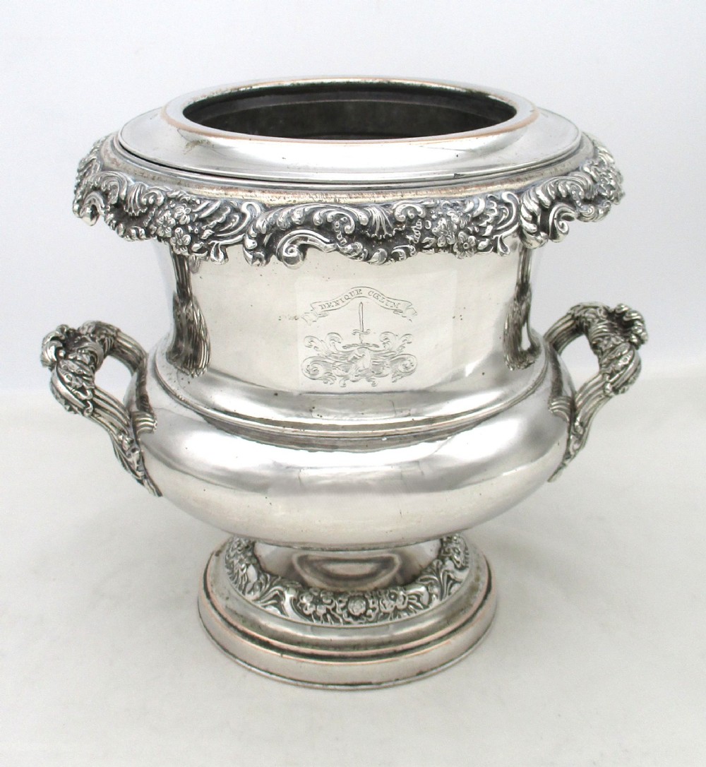A Georgian silver-plated double-handled wine cooler featuring an engraved family crest, foliage borders, and a pedestal base.