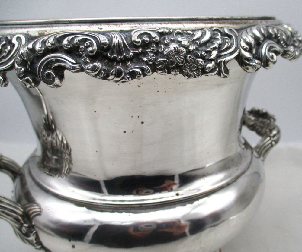 A Georgian silver-plated double-handled wine cooler featuring an engraved family crest, foliage borders, and a pedestal base. View X
