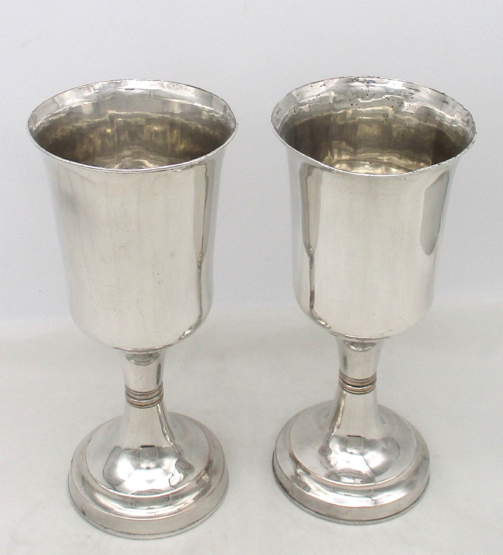 A pair of tall silver-plated church chalices featuring flared rims, knopped central stems, and stepped circular bases.